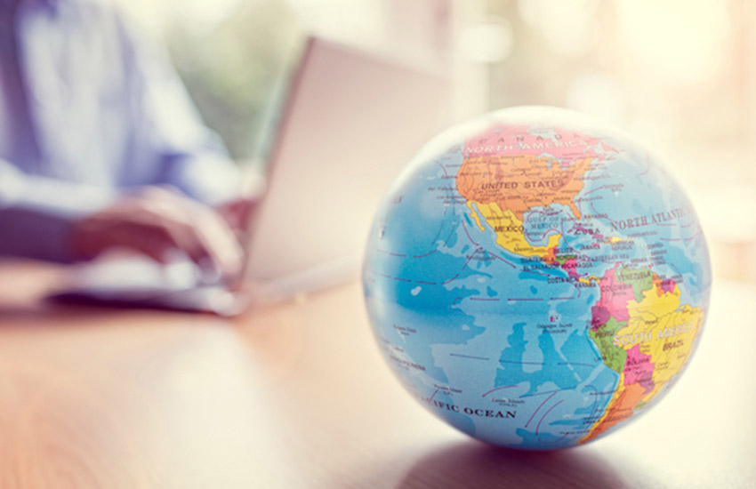 a small globe paper weight on a desk with a blurred person working on a laptop in the background.
