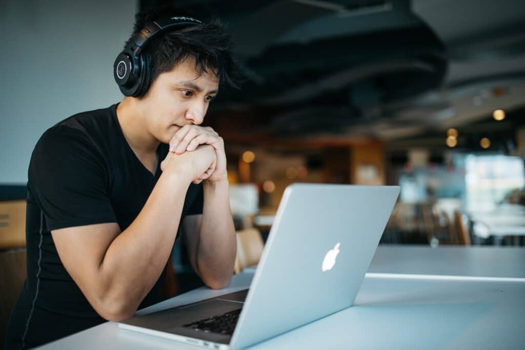 an adult male student wearing headphones looks intently at his laptop screen.