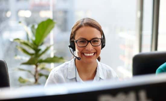 una mujer con un auricular sonriendo sobre el monitor de su computadora portátil.